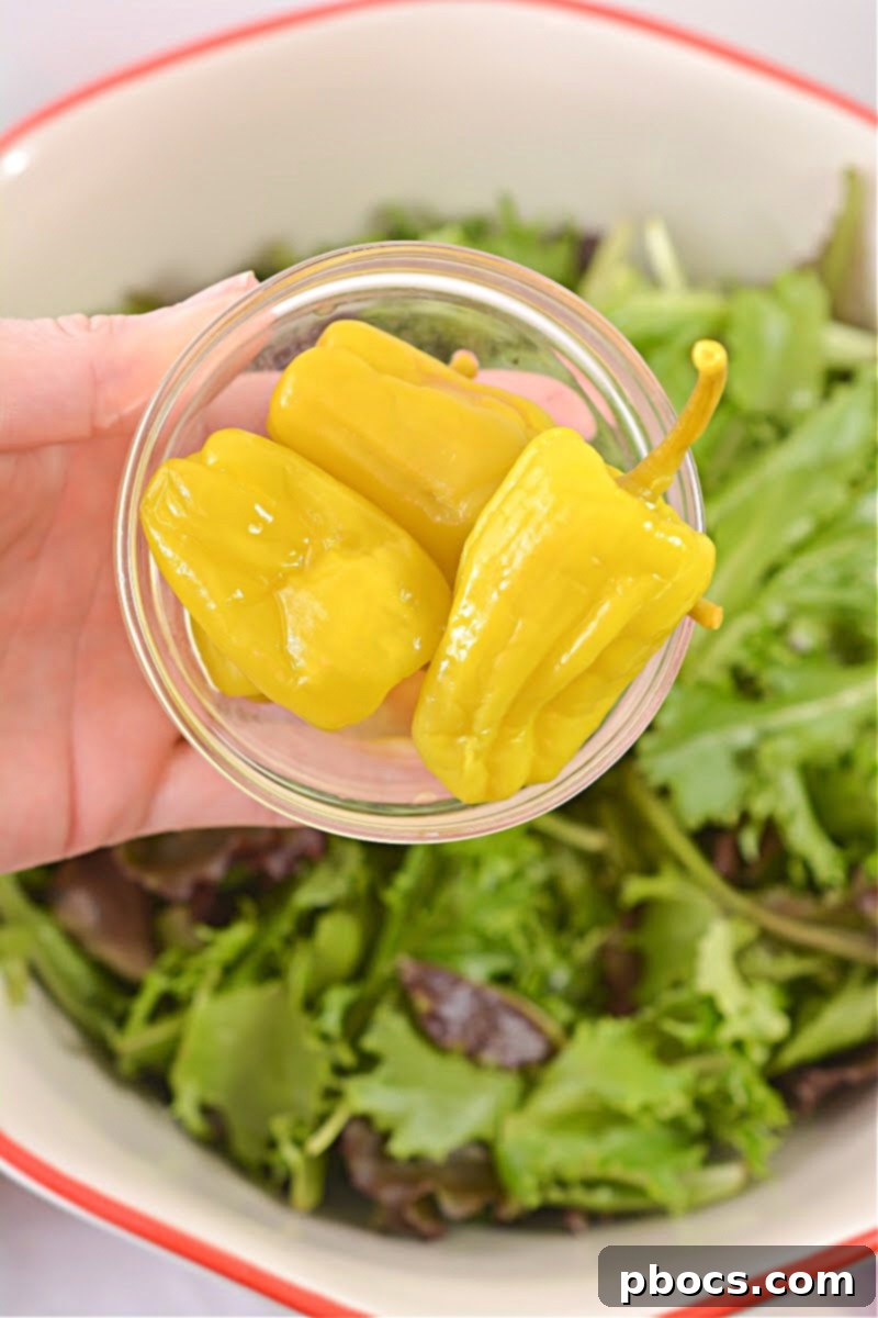 Fresh salad ingredients in a large bowl, including lettuce, tomatoes, red onion, and pepperoncini, ready for the dressing.