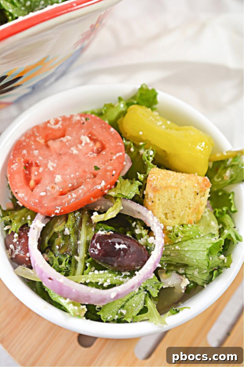A large bowl of Keto Copycat Olive Garden Salad, ready to be tossed, featuring colorful vegetables and a generous sprinkling of parmesan cheese.