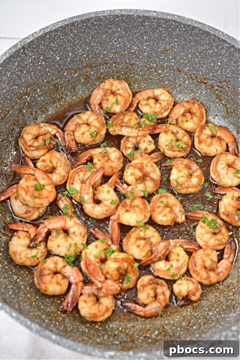 Cooked shrimp being tossed with sugar-free honey in a skillet, creating a beautiful glaze.