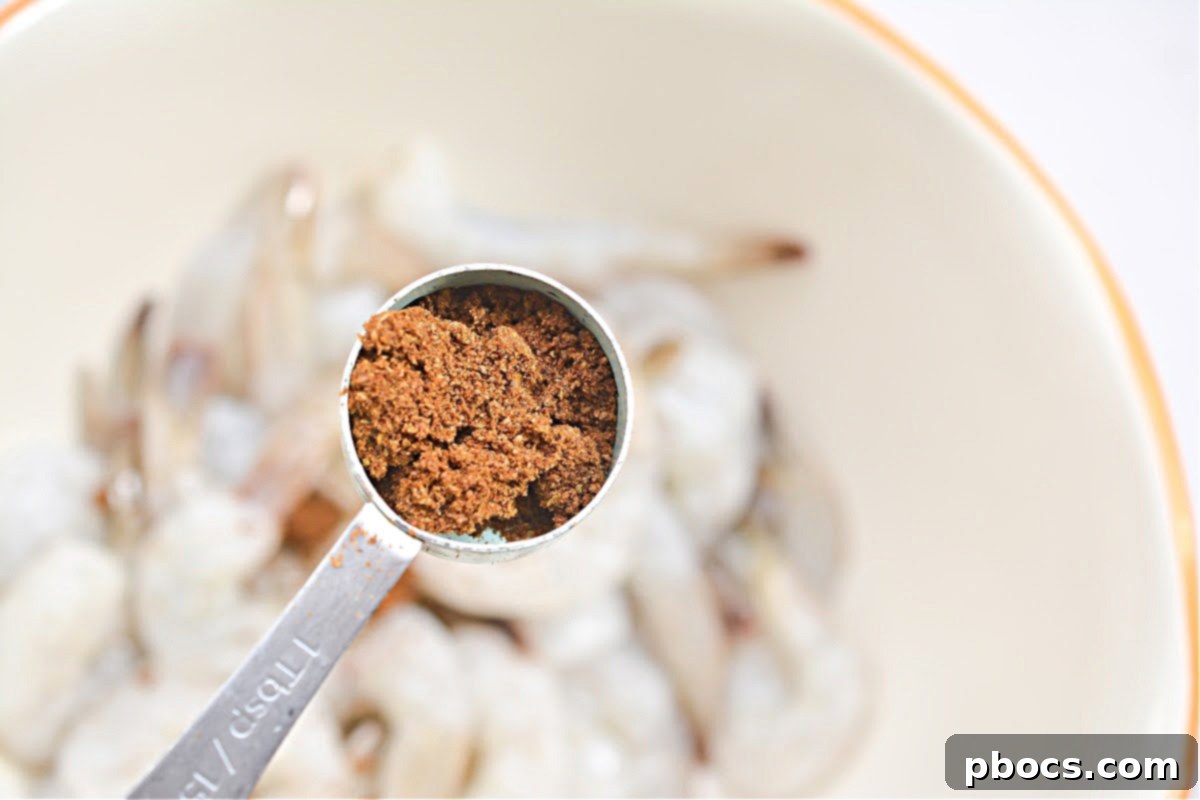 Raw shrimp being tossed thoroughly with Old Bay seasoning in a mixing bowl.