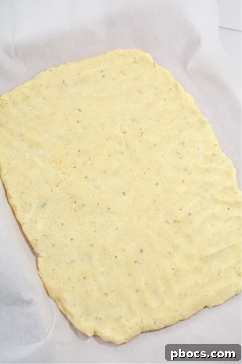 Pressing the fathead dough onto a parchment-lined baking sheet into a rectangular shape.