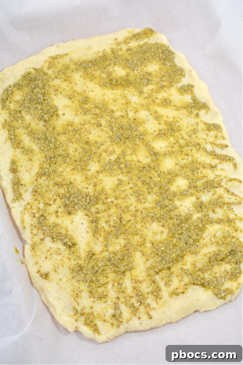Spreading pesto sauce evenly over the pressed fathead dough.