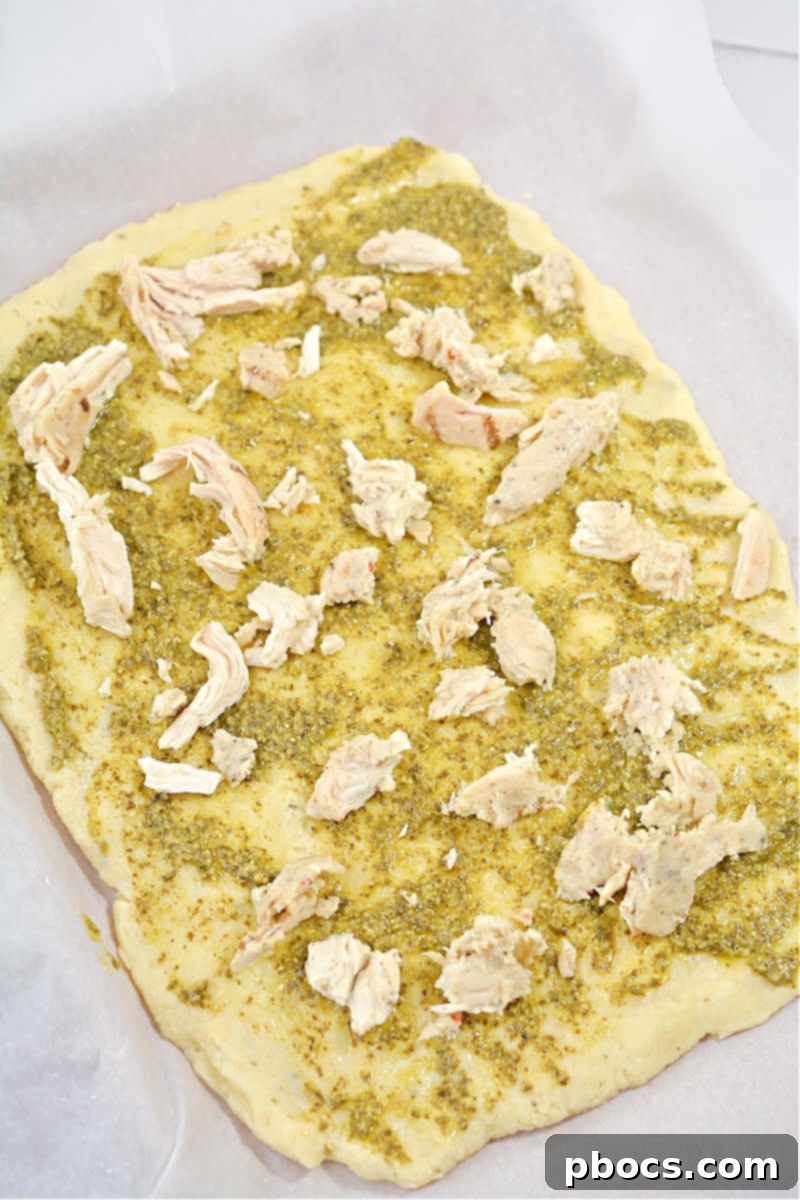 Adding shredded chicken and fresh baby spinach as toppings on the pesto flatbread.
