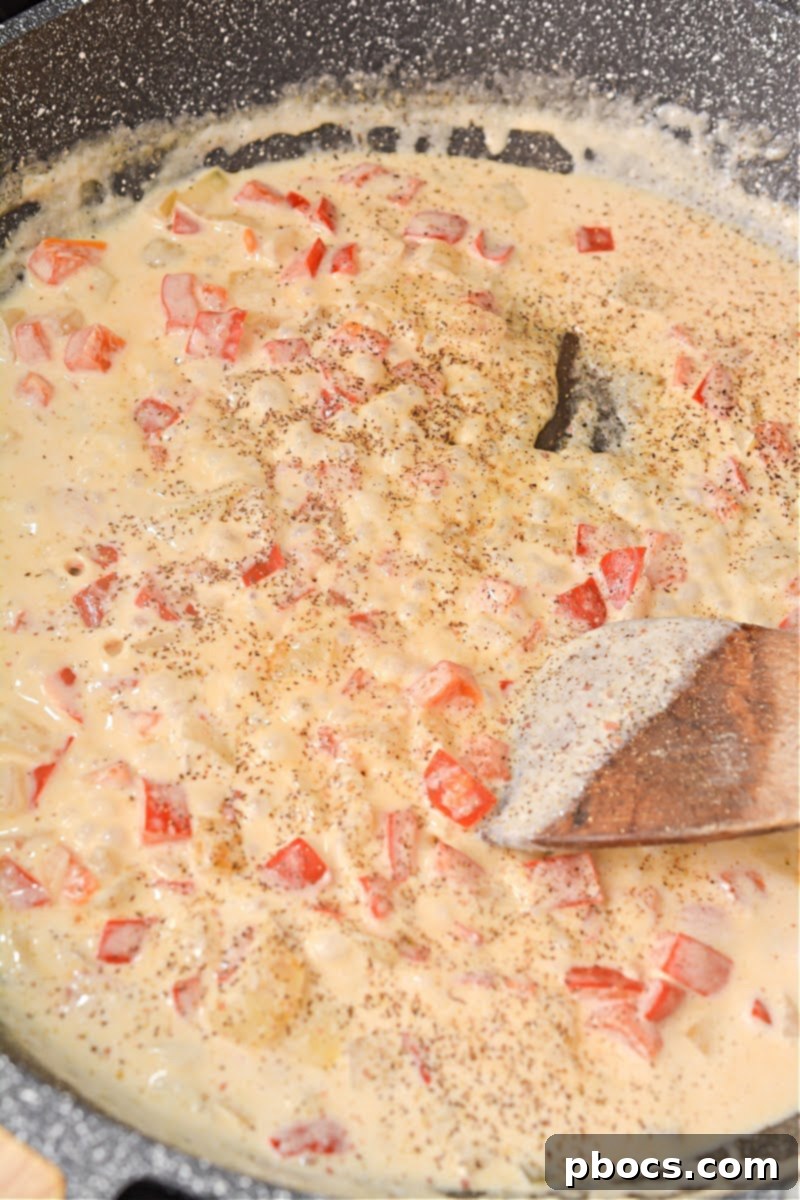 Heavy whipping cream and chicken broth simmering in a skillet with sautéed vegetables, thickening into a creamy sauce.