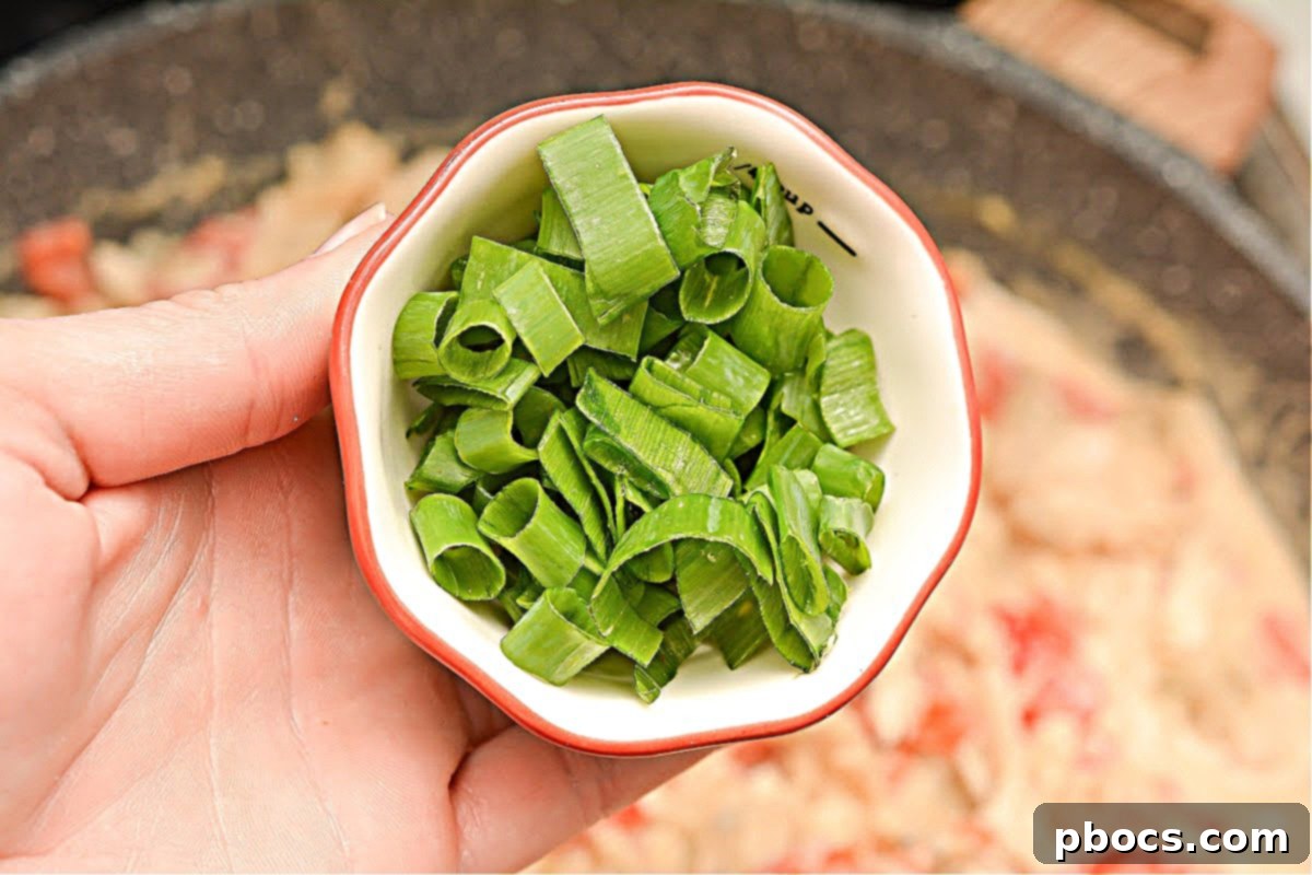 Shredded chicken and chopped green onions mixed into the creamy, spicy sauce in the skillet.