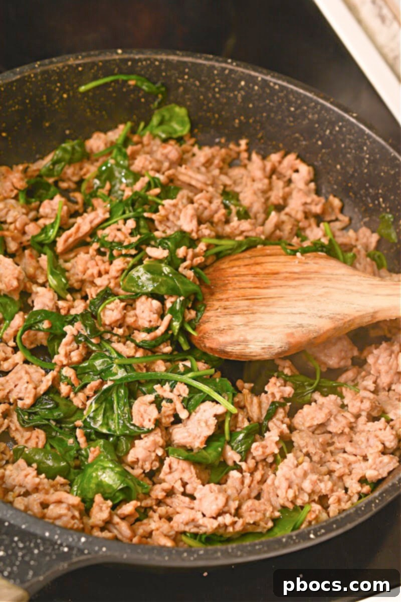 Hearty Keto Sausage Stuffed Bell Peppers 11 Adding spinach to cooked sausage in a skillet