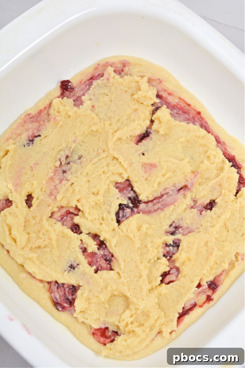 Swirling raspberry jam over cake batter in a baking dish.