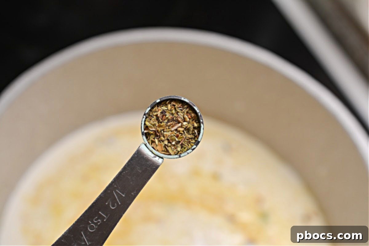 Oregano and seasoning being stirred into the simmering soup base.