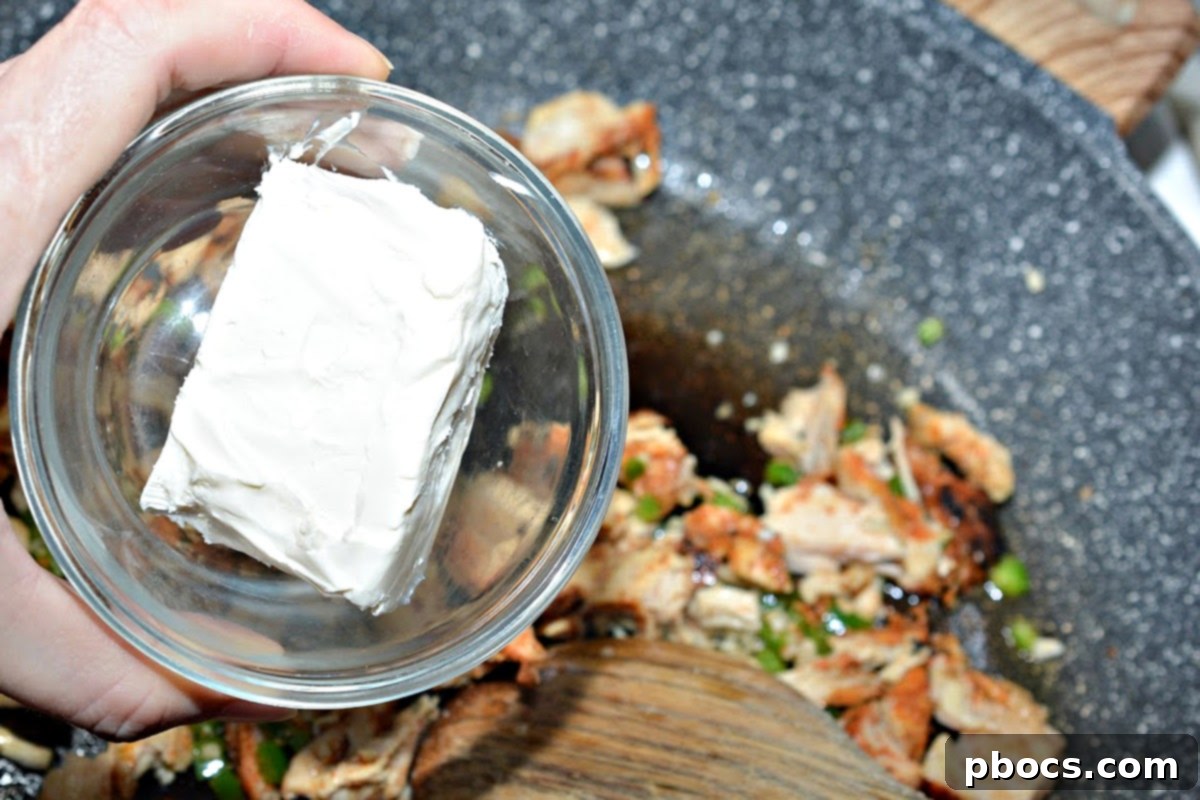 Shredded chicken, cream cheese, and ranch seasoning being stirred into the skillet.