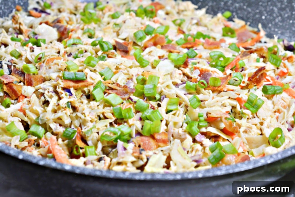 Crumbled bacon being stirred into the finished Keto Crack Slaw.