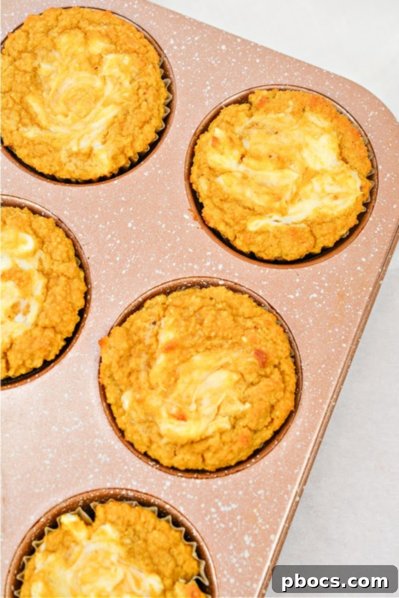 Keto Pumpkin Muffins with Cream Cheese Swirl 4 Freshly baked Keto Pumpkin Cream Cheese Swirl Muffins arranged on a cooling rack