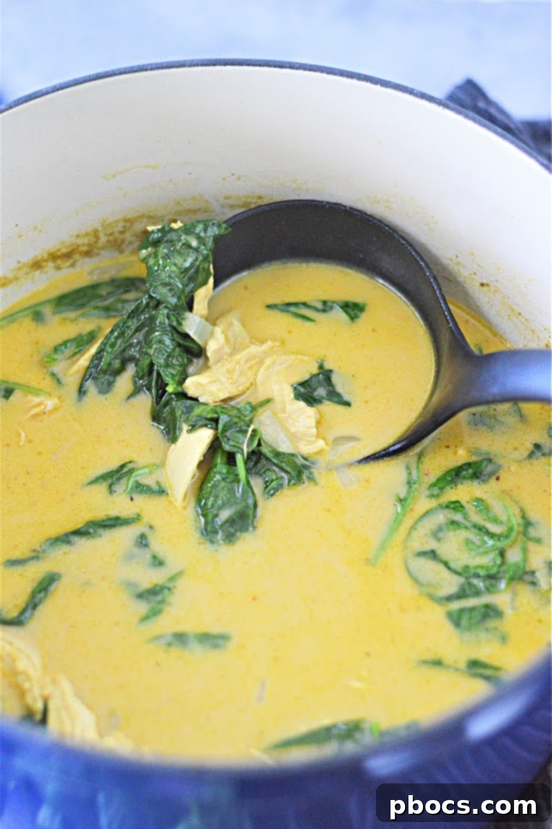 Stirring spinach and heavy cream into the simmering keto pumpkin curry soup