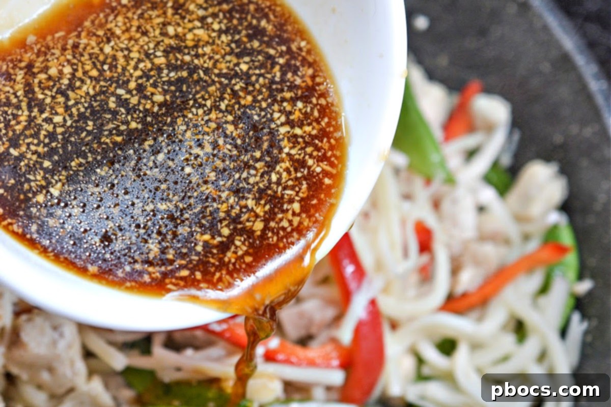 Pouring the savory sauce over the chow mein ingredients in the pan.