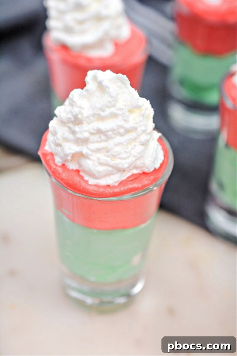 Decadent Keto White Chocolate Christmas Shooters 15 Piping red keto white chocolate cream on top of green in shot glasses.