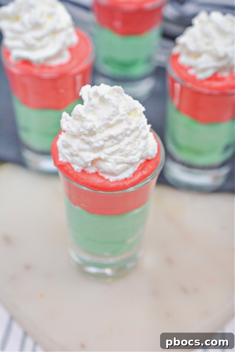Decadent Keto White Chocolate Christmas Shooters 6 A hand piping green keto white chocolate mixture into a shot glass, showing the creamy texture.