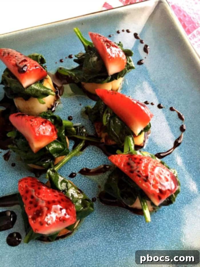 A beautifully plated dish of pan-seared scallops on a bed of wilted spinach, garnished with fresh strawberries and a rich balsamic glaze.