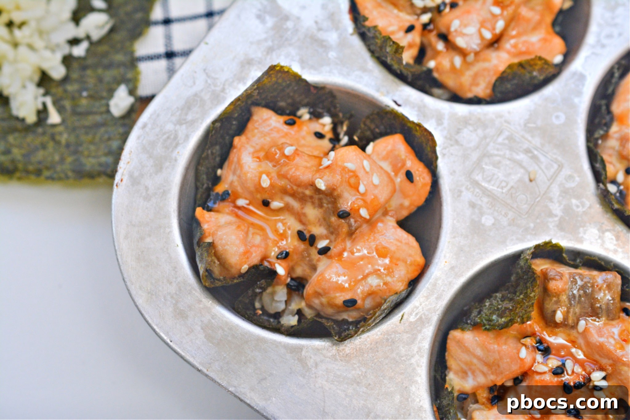 Deliciously cooked Keto TikTok Salmon Sushi Nori Cups in a muffin tin, drizzled with sauce and sprinkled with sesame seeds