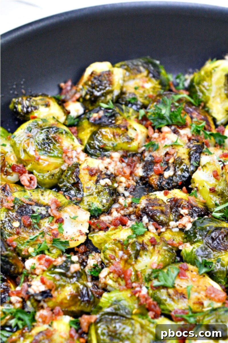 A skillet filled with freshly cooked Keto Smashed Brown Butter Brussels Sprouts, garnished with bacon and red pepper flakes.