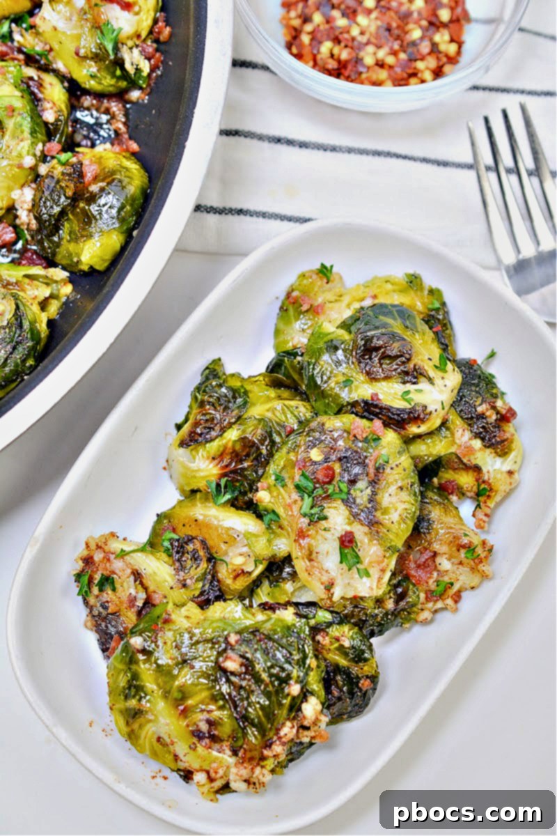 A pristine plate of Keto Smashed Brown Butter Brussels Sprouts, garnished with bacon and red pepper flakes, showcasing its delicious appeal.