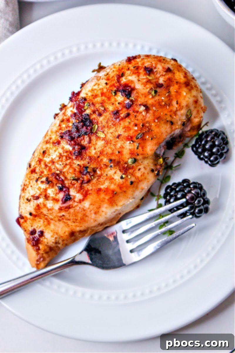A blackberry chicken breast on a white plate with a fork and two blackberries