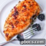 A blackberry chicken breast on a white plate with a fork and two blackberries