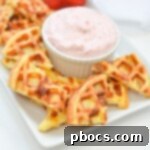 Strawberry Shortcake Chaffle Dippers with Keto Cream Dream 14 A plate of chaffle chips with three strawberries on it with a bowl of strawberry dip