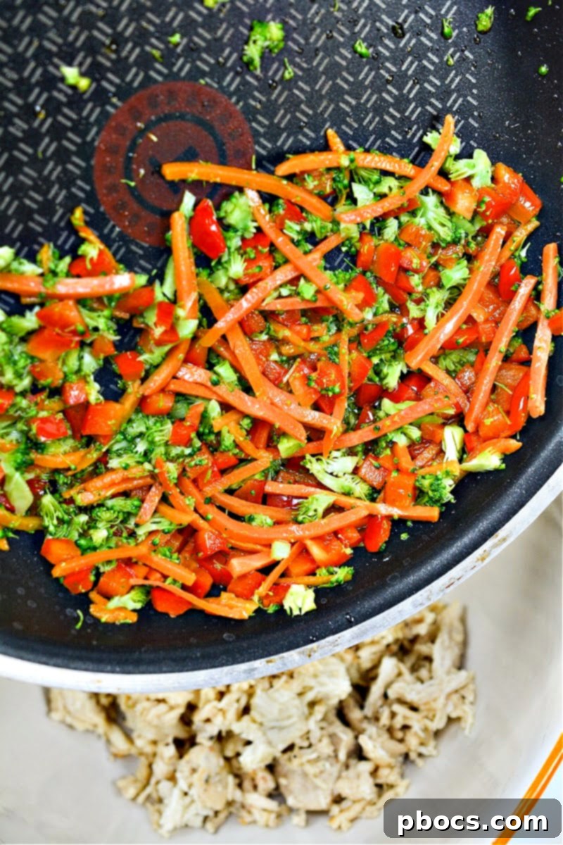 Sauteed carrots, red bell peppers, and broccoli florets cooking in a skillet.