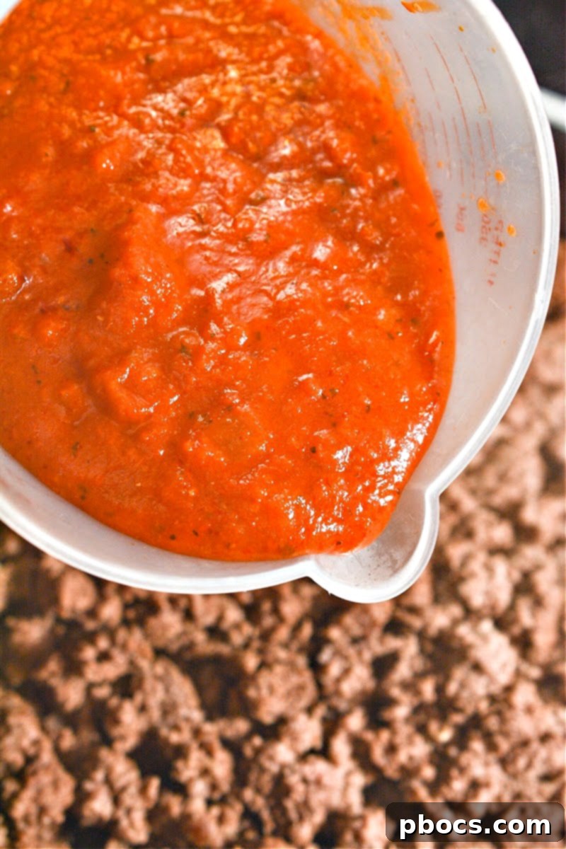 Marinara sauce being added to cooked ground beef in a skillet