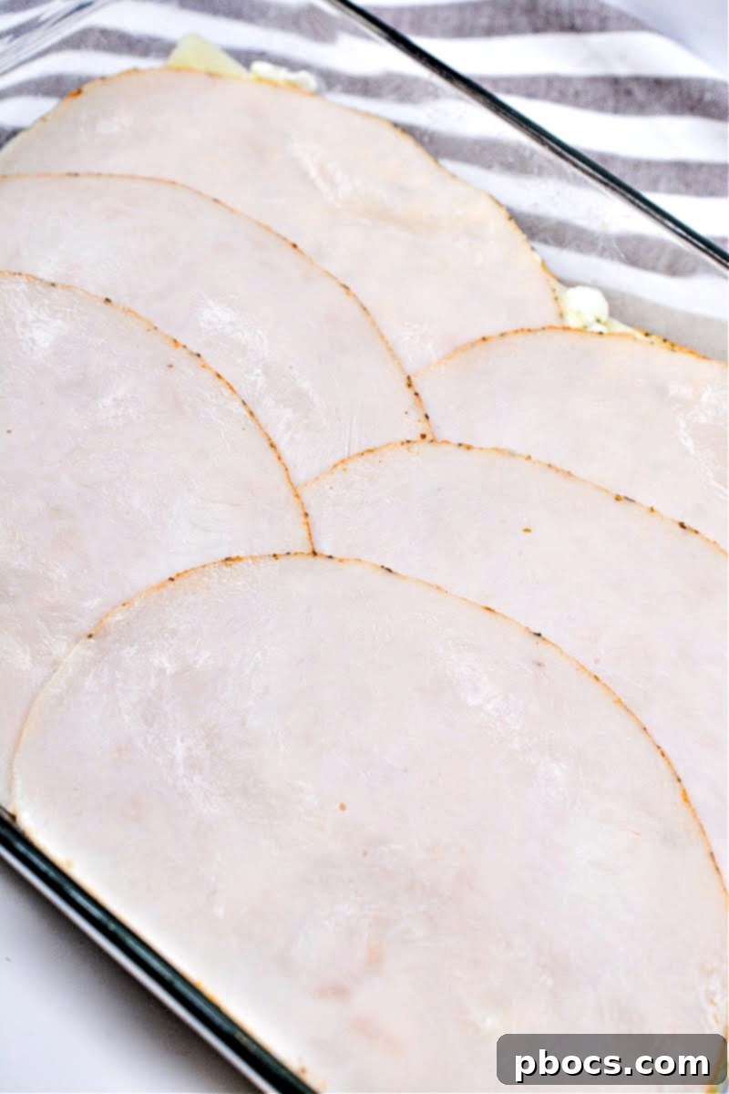 Layering sliced deli turkey meat over the meat sauce in a baking dish