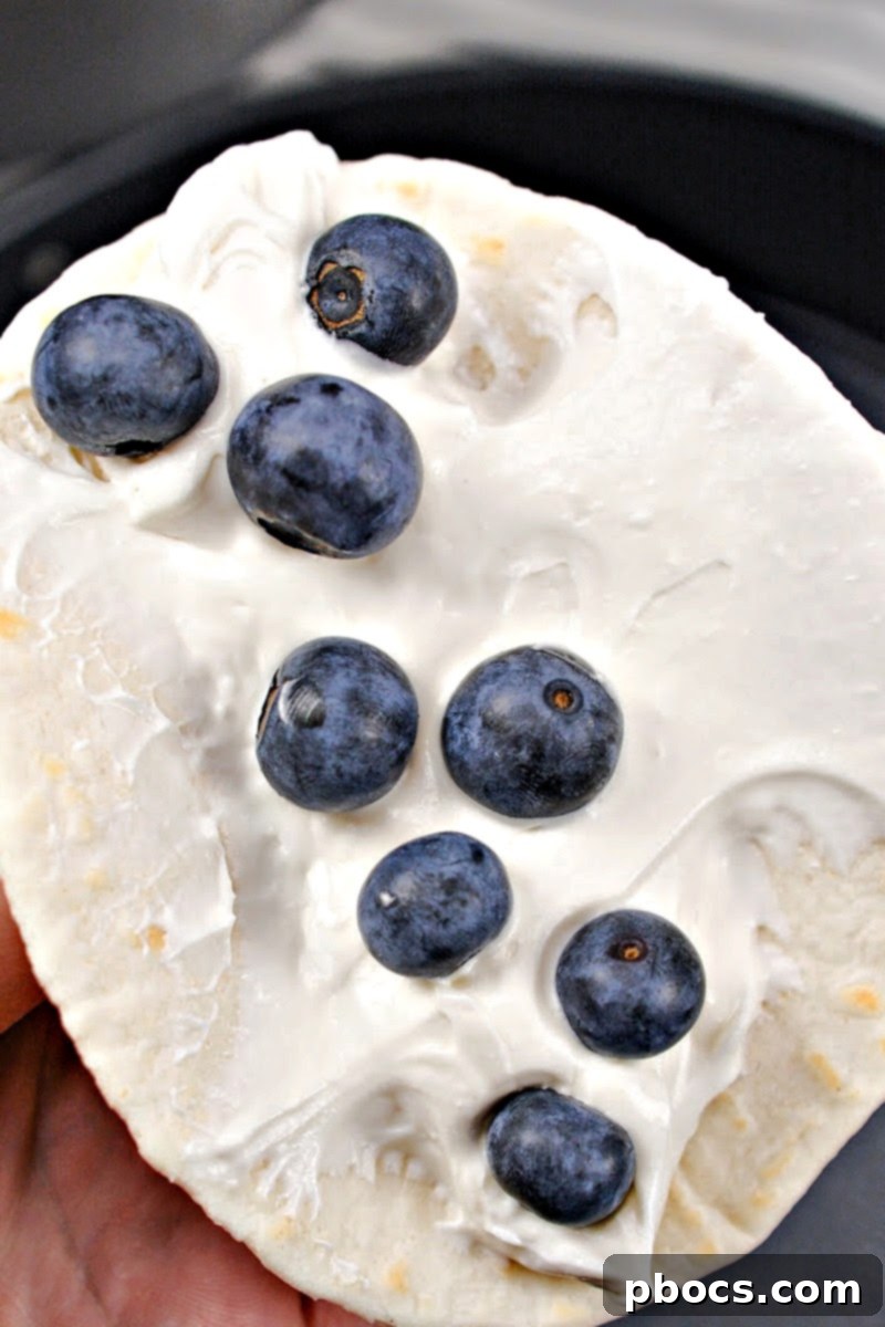 Adding fresh blueberries on top of the cream cheese layer on a tortilla