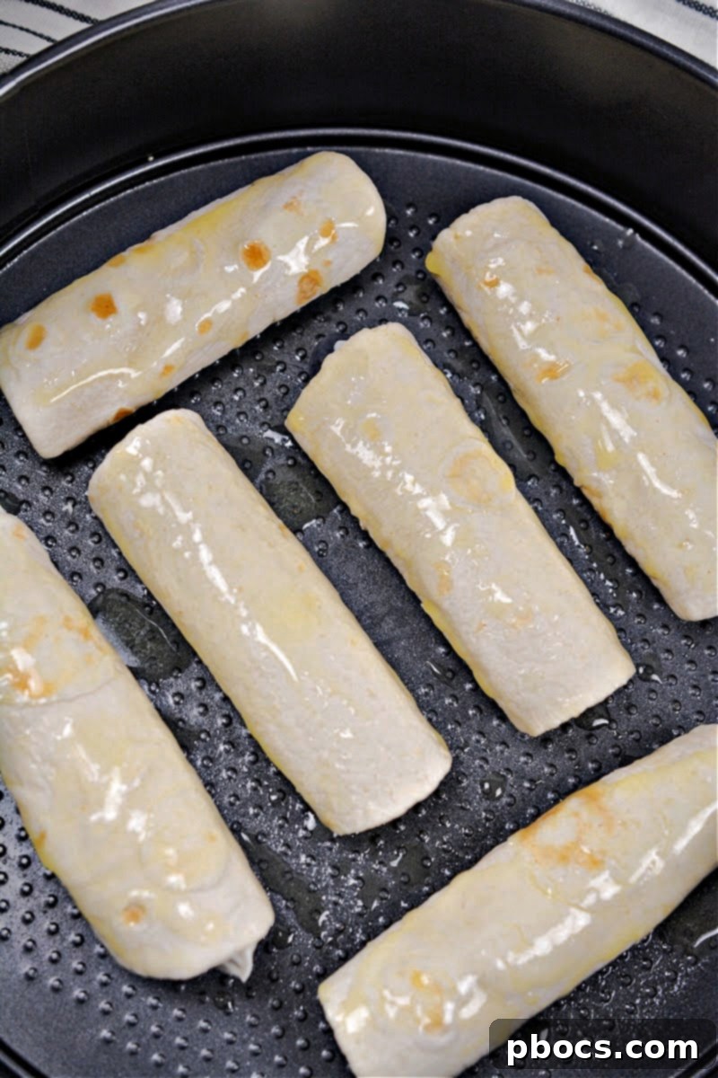Unbaked Crispy Keto Blueberry Cream Cheese Roll-Ups placed seam-side down in an air fryer basket