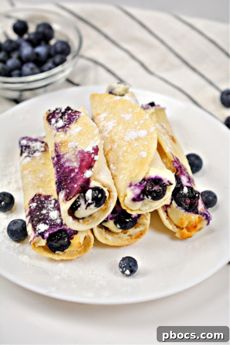 Crispy Keto Blueberry Cream Cheese Roll-Ups on a white plate, with a bowl of fresh blueberries in the background