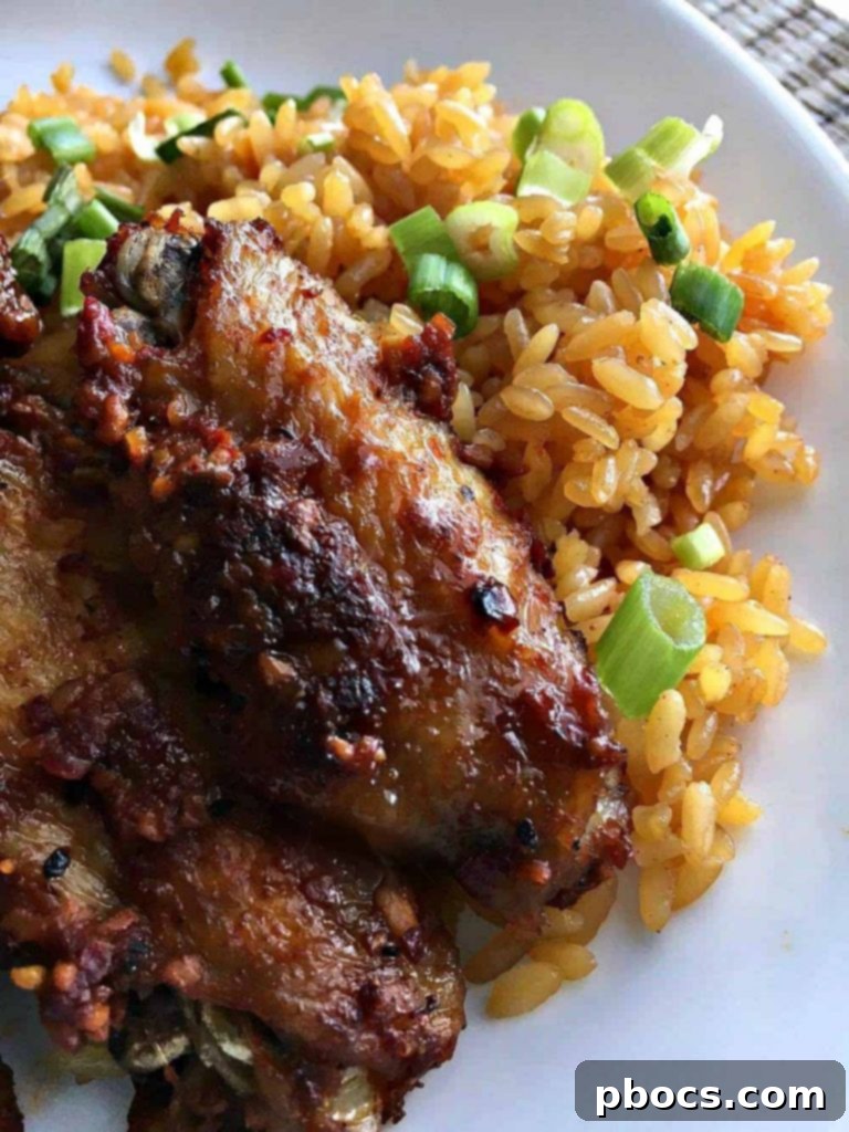 A plate of perfectly cooked honey garlic pepper wings with a side of yellow rice.