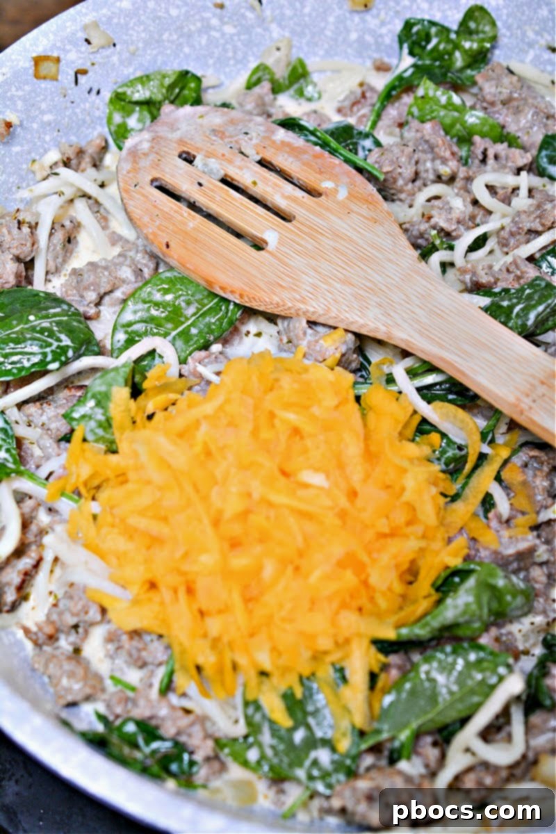 Shredded butternut squash and fresh spinach added to the creamy sauce in the skillet.