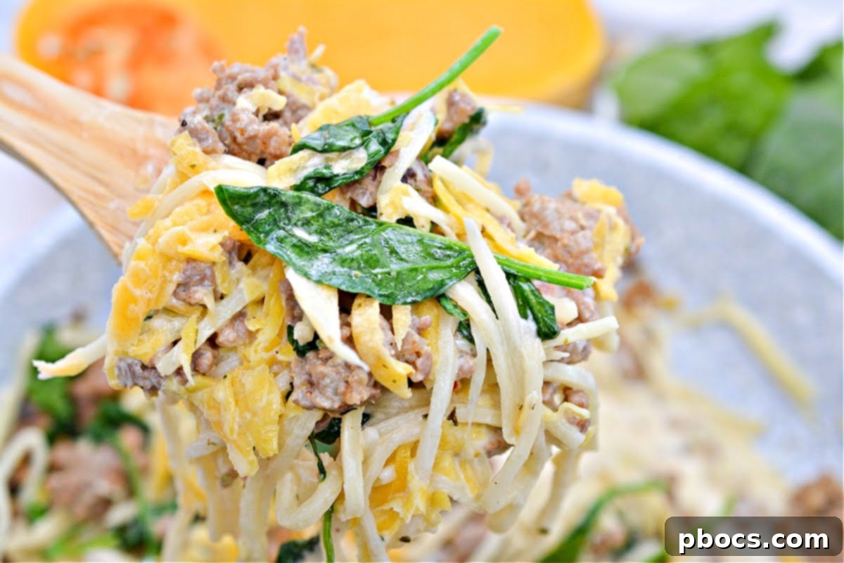 A spoon serving a generous portion of butternut squash, sausage, and Palmini noodles from a skillet.
