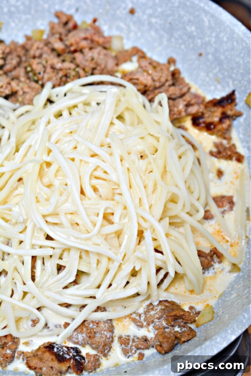 Palmini noodles being added to the sautéed sausage and onion mixture in a skillet.