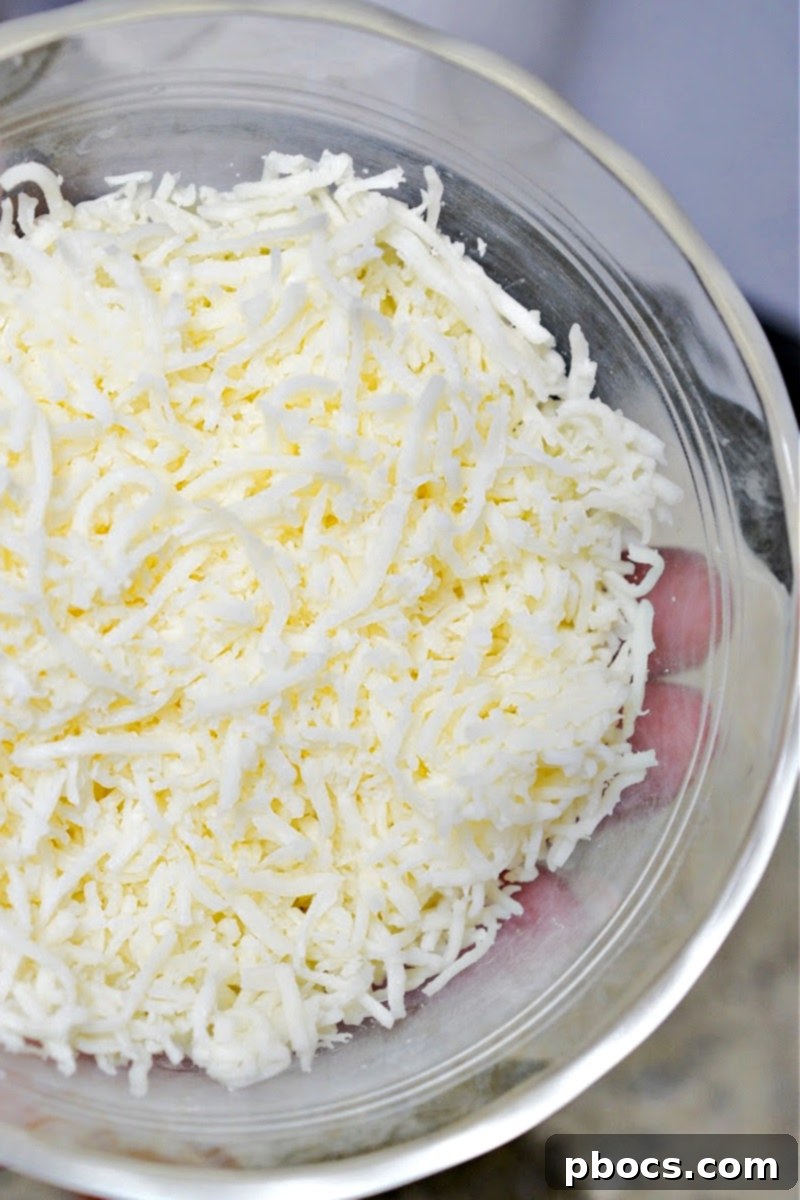 Shredded mozzarella cheese melting into a creamy sauce in a skillet.