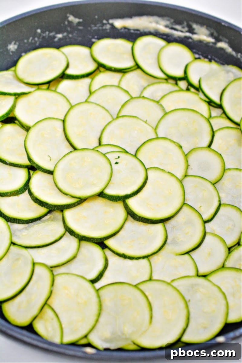 Thinly sliced zucchini being arranged in overlapping circles in a skillet.