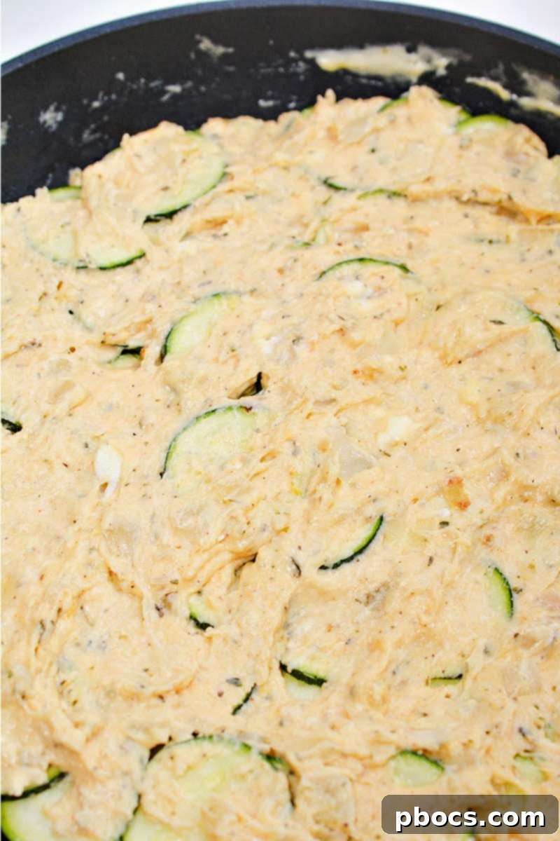 Uncooked Keto Scalloped Zucchini in a skillet, with the sauce poured over the zucchini layers.