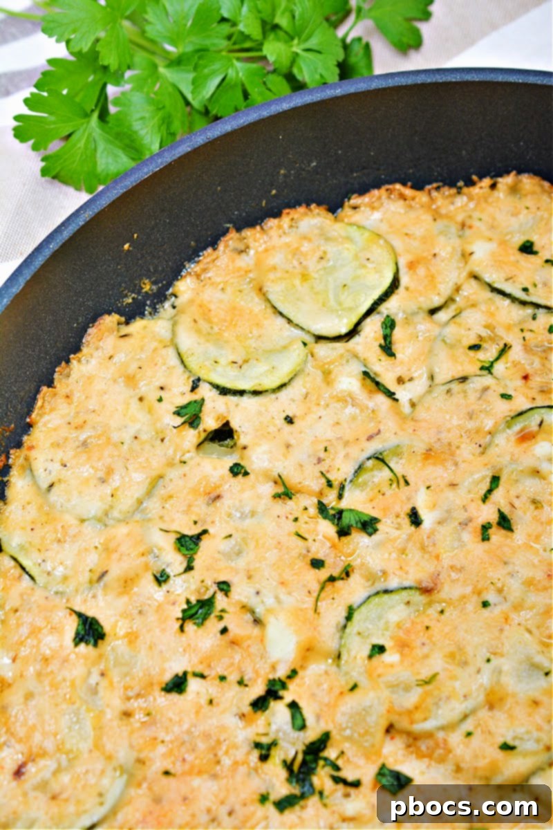 Keto Scalloped Zucchini in a cast iron skillet, showcasing layers of thinly sliced zucchini and creamy cheese sauce.