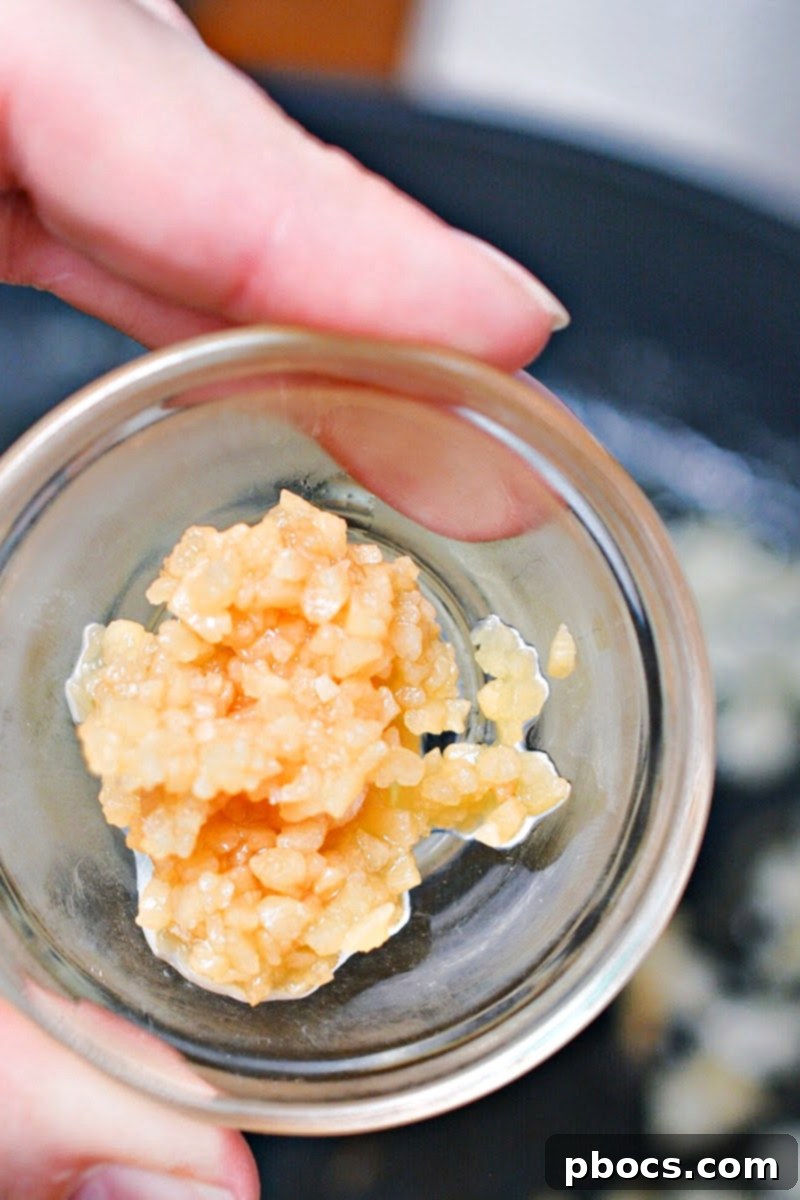 Minced garlic being added to the sautéed onions in a skillet.