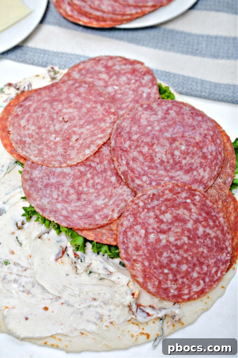 Keto Italian Swirls 13 Layering lettuce, pepperoni, and salami over the cheese on a tortilla.