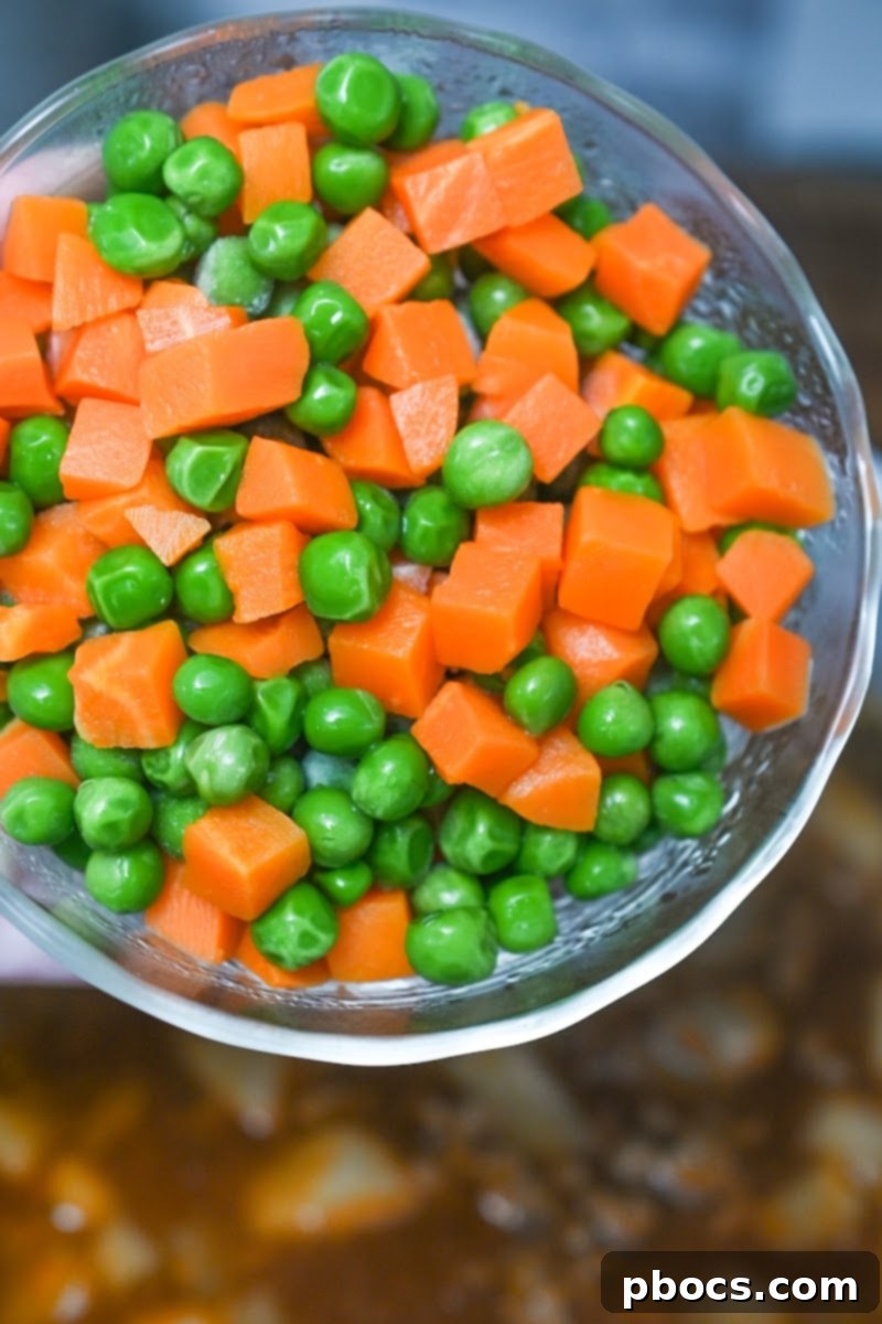 Adding frozen peas, carrots, and heavy cream to the simmering soup
