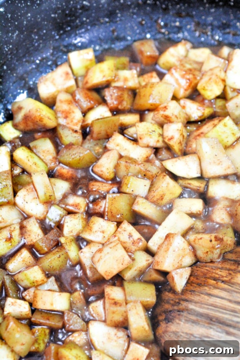 Diced zucchini cooking in a skillet with butter, brown Swerve, vanilla, apple pie spice, and water.