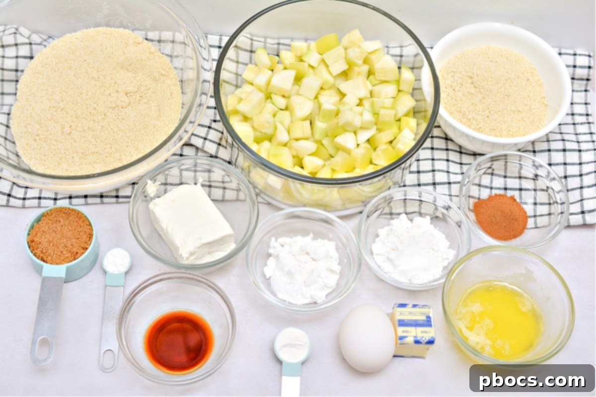 All the ingredients for Keto Apple Pie laid out on a kitchen counter: almond flour, cream cheese, zucchini, butter, Swerve, vanilla, apple pie spice, and eggs.