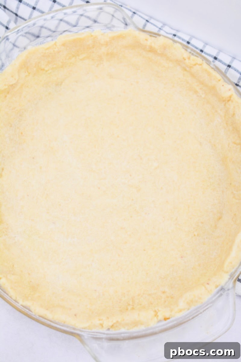 The keto pie crust mixture pressed firmly into the bottom and sides of a pie plate, ready for baking.