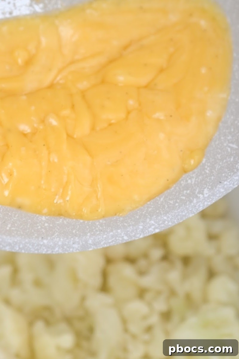 Whisking shredded cheddar cheese into cream sauce