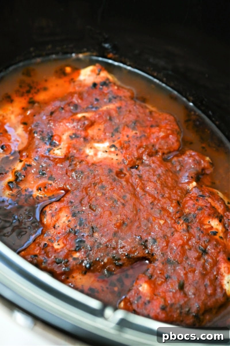 Keto Crockpot Tomato Alfredo Chicken, adding Parmesan cheese.