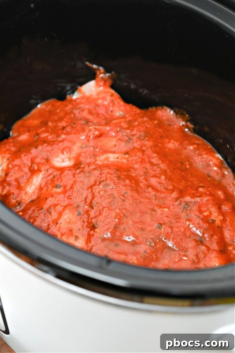 Keto Crockpot Tomato Alfredo Chicken, adding marinara sauce.