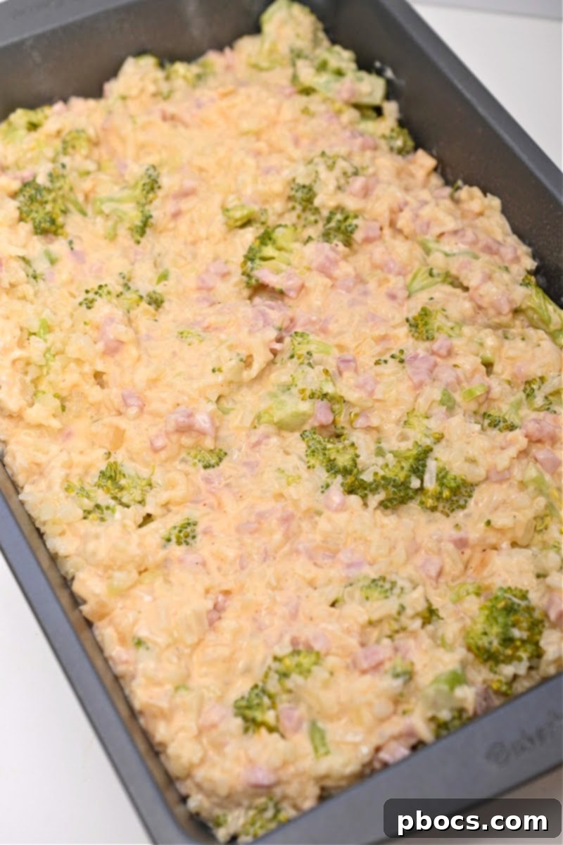 Pouring cheese sauce over cauliflower rice, broccoli, and ham
